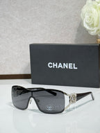 Sunglasses with dark lenses, black frame, ornate silver-toned bridge charm