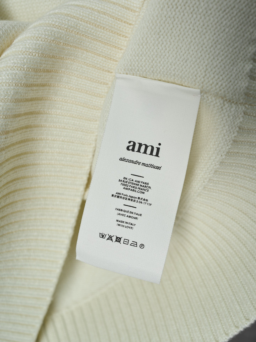 Cream knit sweater with attached interior brand label reading “ami”