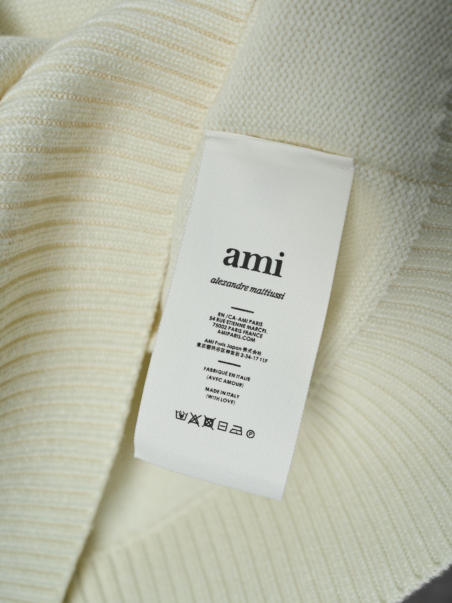 Cream knit sweater with attached interior brand label reading “ami”