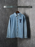 Light blue denim button-up shirt with pointed collar and dark heart-and-ribbon applique