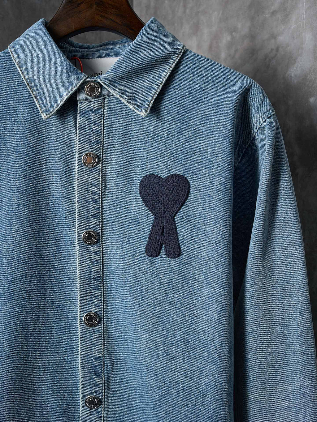 Light blue denim shirt front view with pointed collar and dark heart-and-ribbon patch