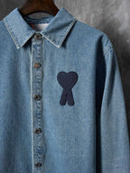 Light blue denim shirt front view with pointed collar and dark heart-and-ribbon patch