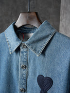 Denim shirt collar detail with dark heart-and-ribbon patch and metal snap buttons