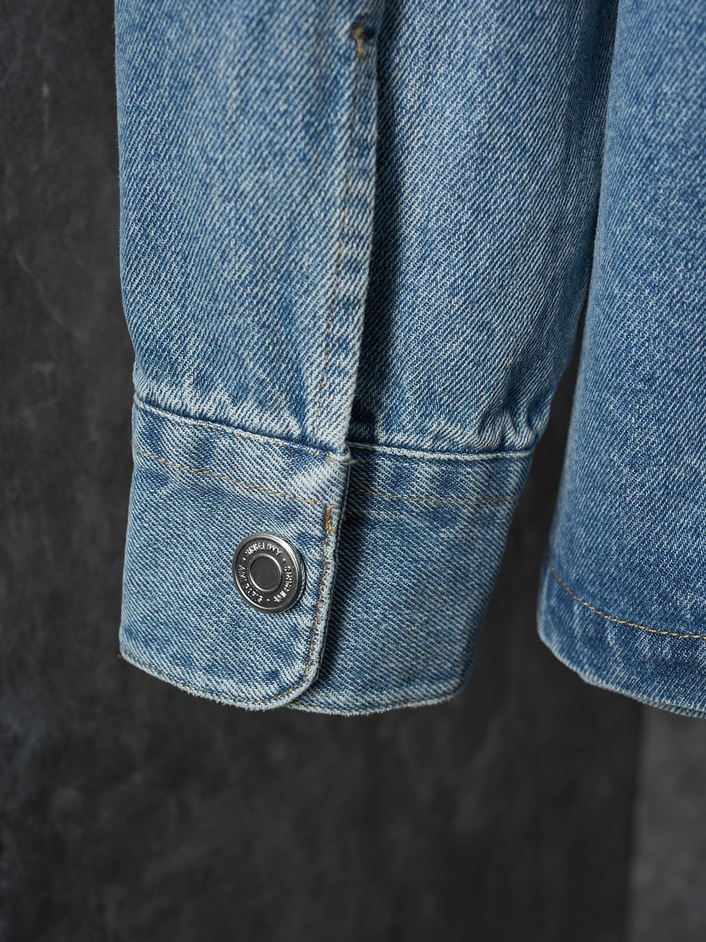 Denim shirt cuff detail with metal snap button at lower edge