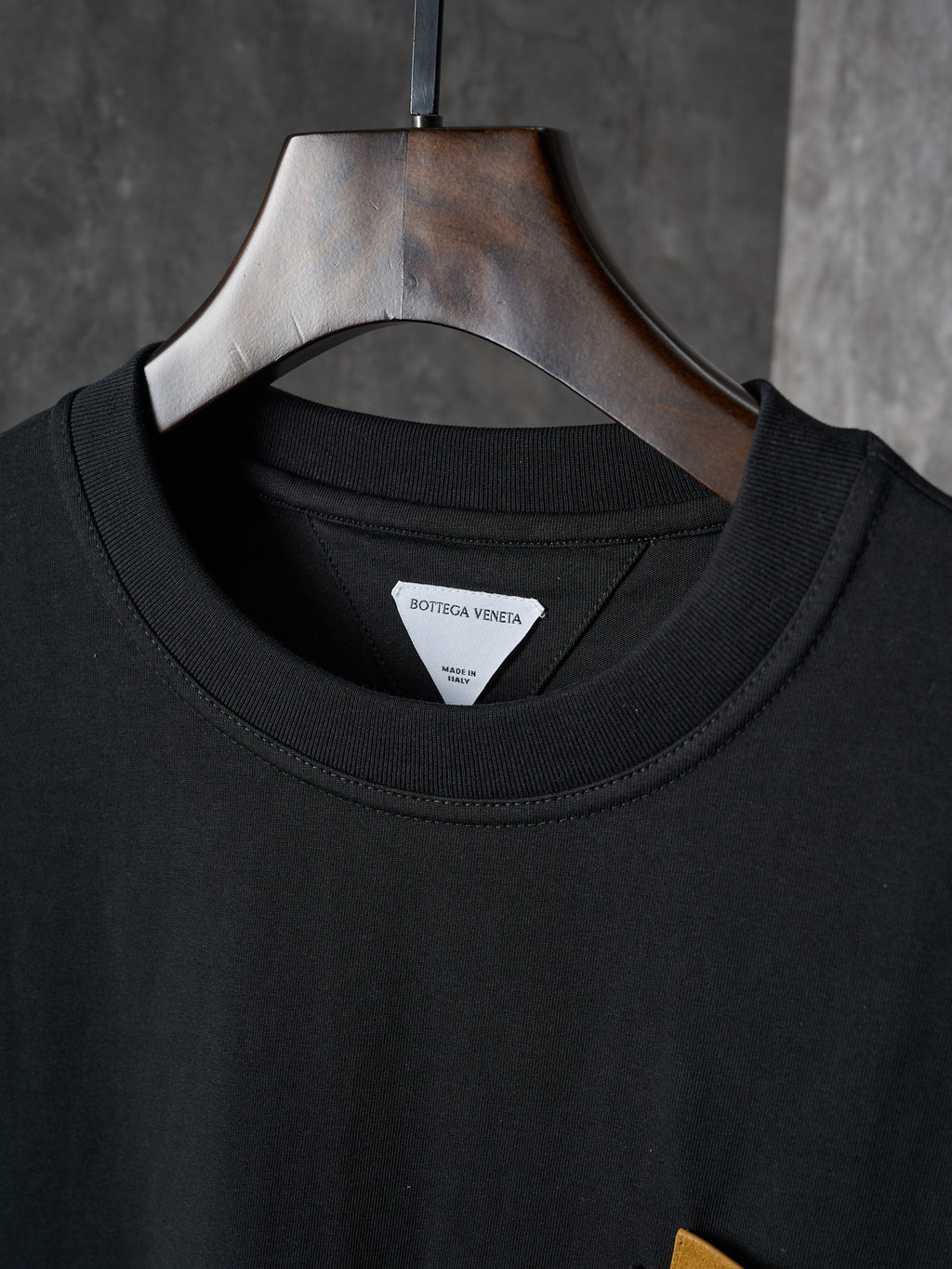 Black crewneck T-shirt with inner neckline label, hung on a wooden hanger
