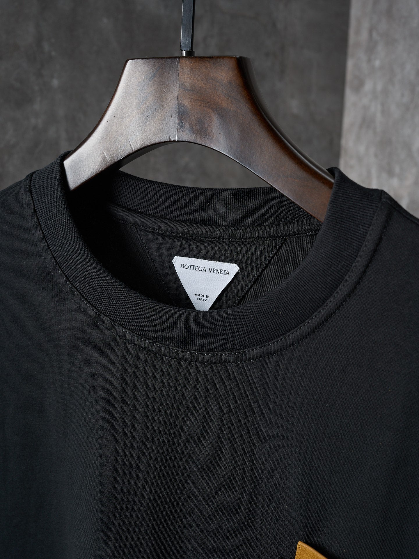 Black crewneck T-shirt with inner neckline label, hung on a wooden hanger