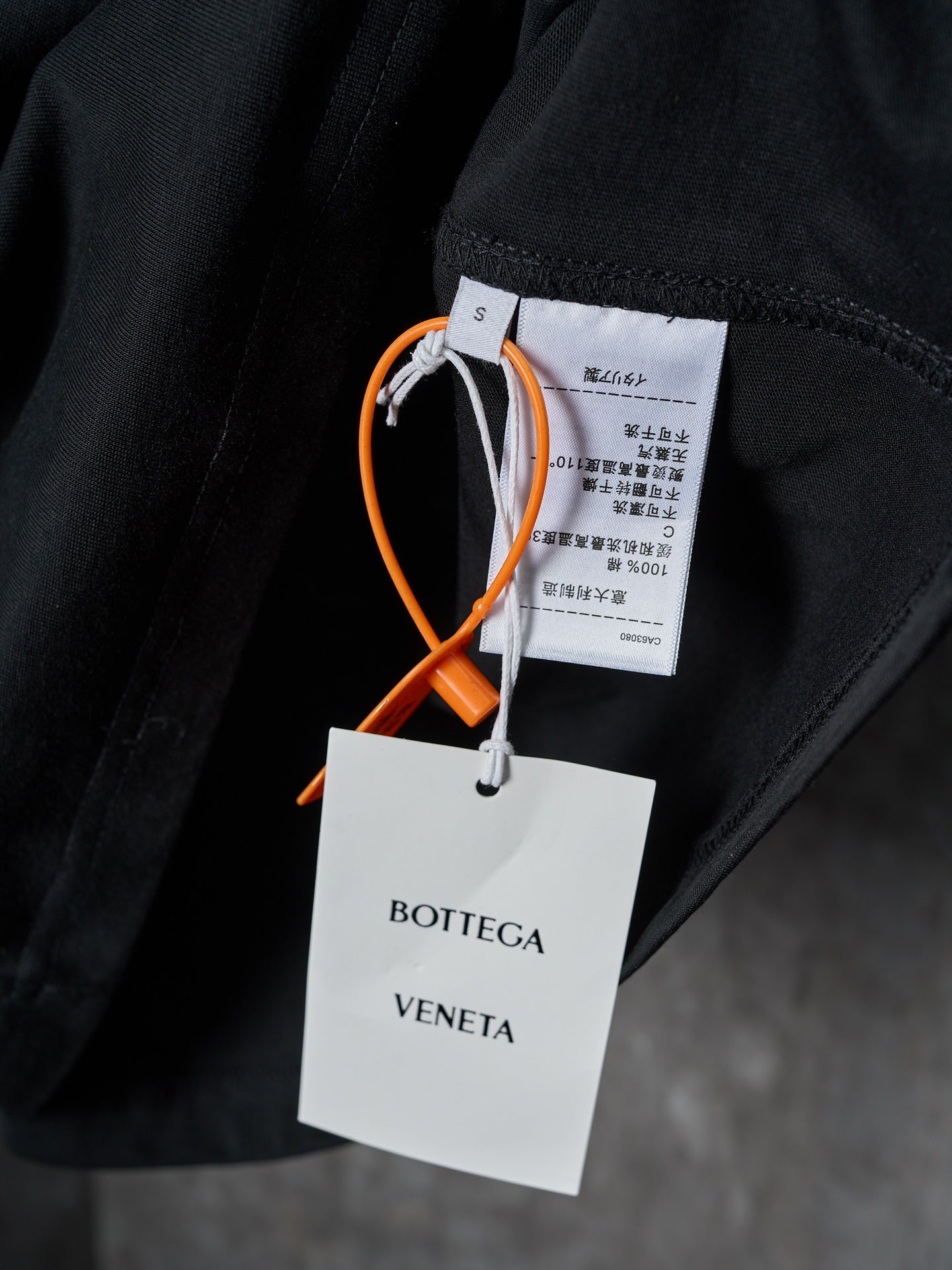 Black T-shirt with attached fabric tag and white brand tag labeled Bottega Veneta