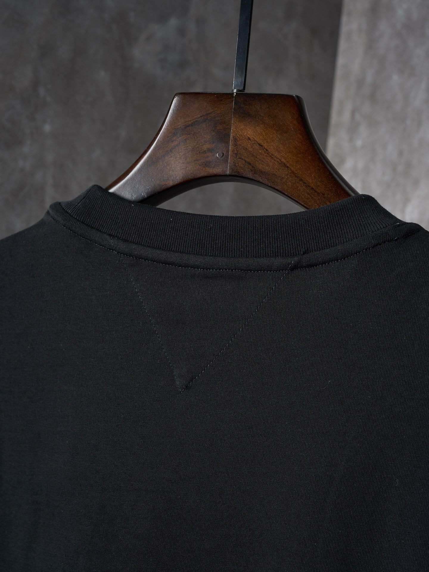 Black T-shirt neckline and back collar seam, hung on a wooden hanger