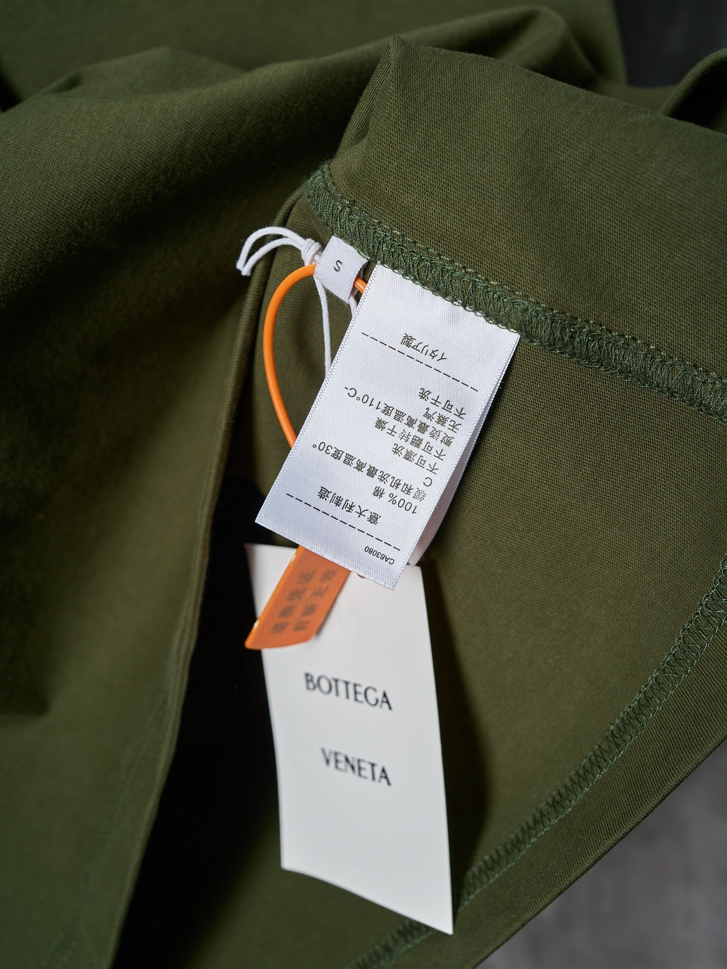 Olive green T-shirt with hanging retail tags and orange brand tag