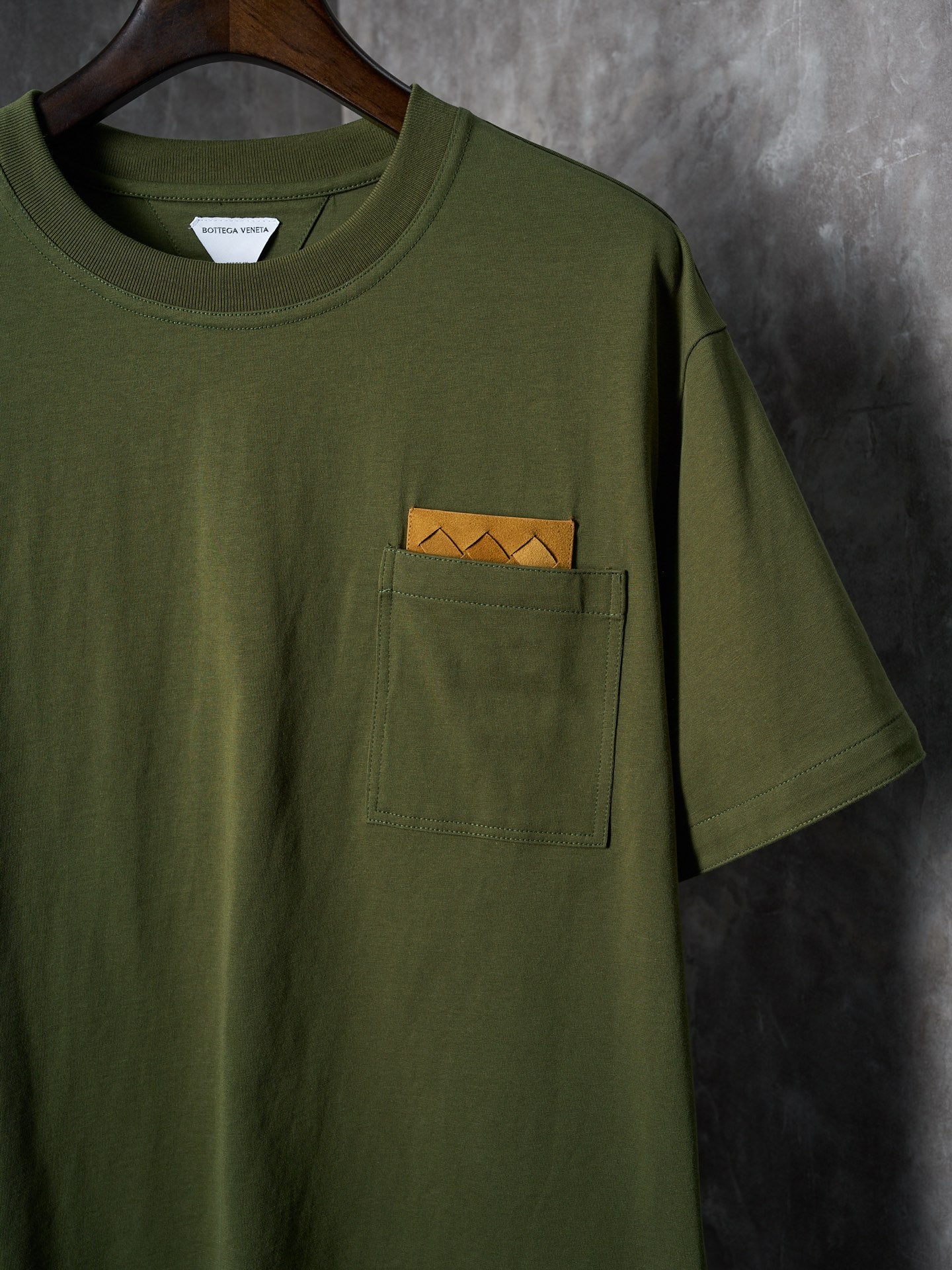 Olive green T-shirt with front chest pocket and orange logo tag