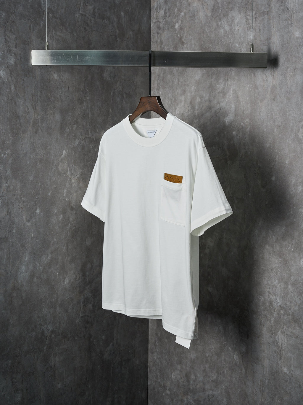 Off-white T-shirt with chest pocket and brown embroidered patch, front view on hanger