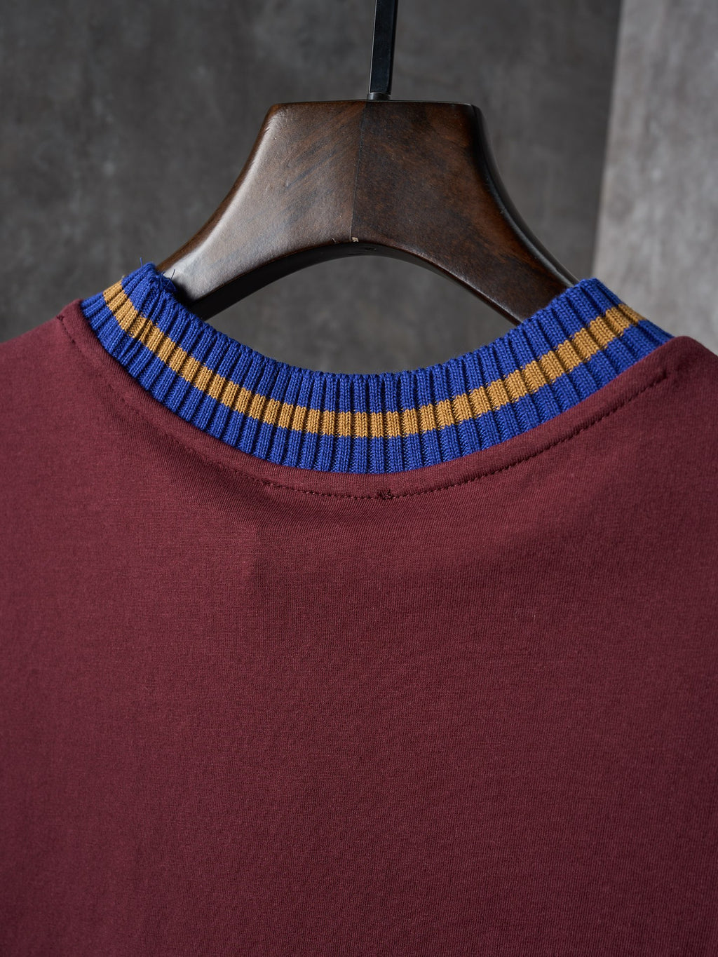 Burgundy T-shirt neckline close-up with blue and yellow striped ribbed collar
