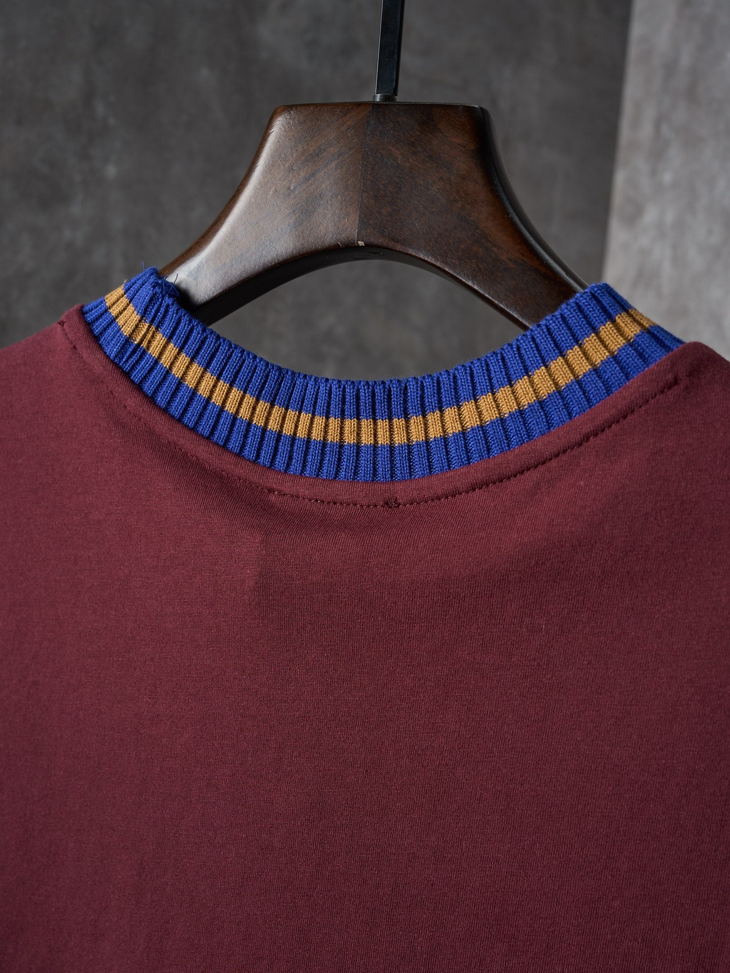 Burgundy T-shirt neckline close-up with blue and yellow striped ribbed collar
