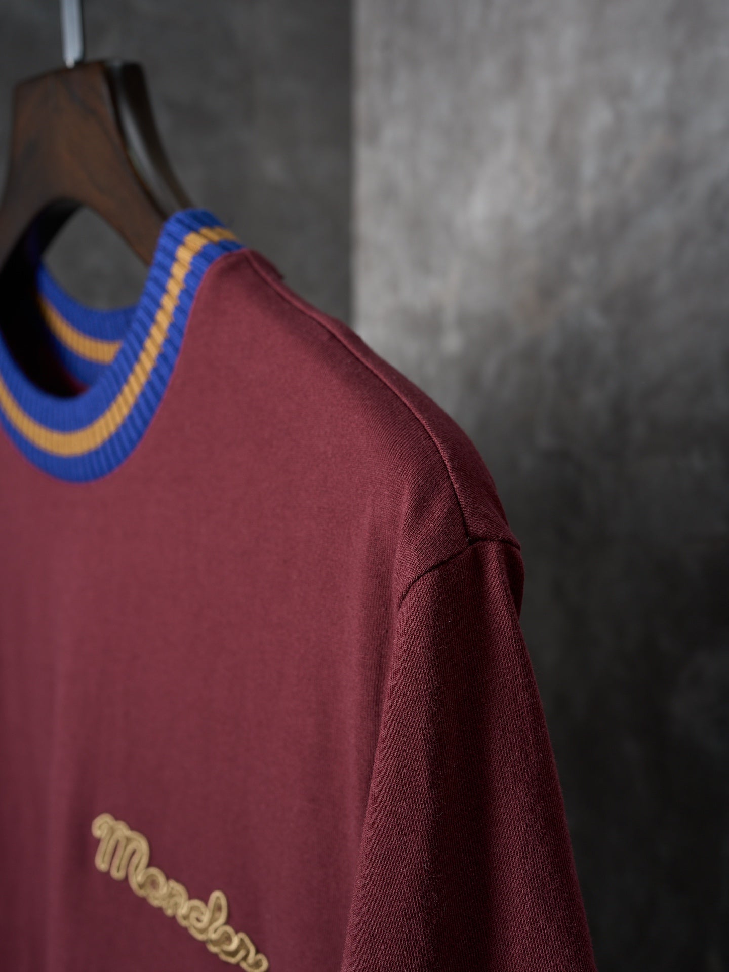 Burgundy T-shirt side view with striped crew neck and gold script logo