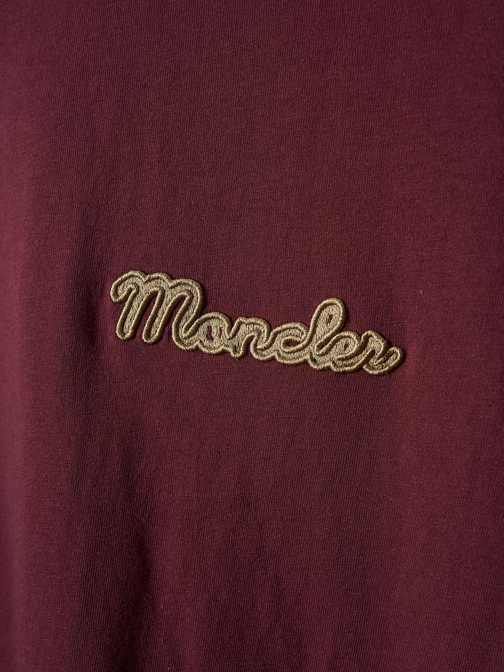 Close-up of burgundy T-shirt front with gold embroidered “Moncler” logo