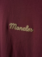 Close-up of burgundy T-shirt front with gold embroidered “Moncler” logo