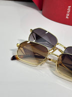 Prada sunglasses close-up, gold frames with dark lenses, beside a red logo case.