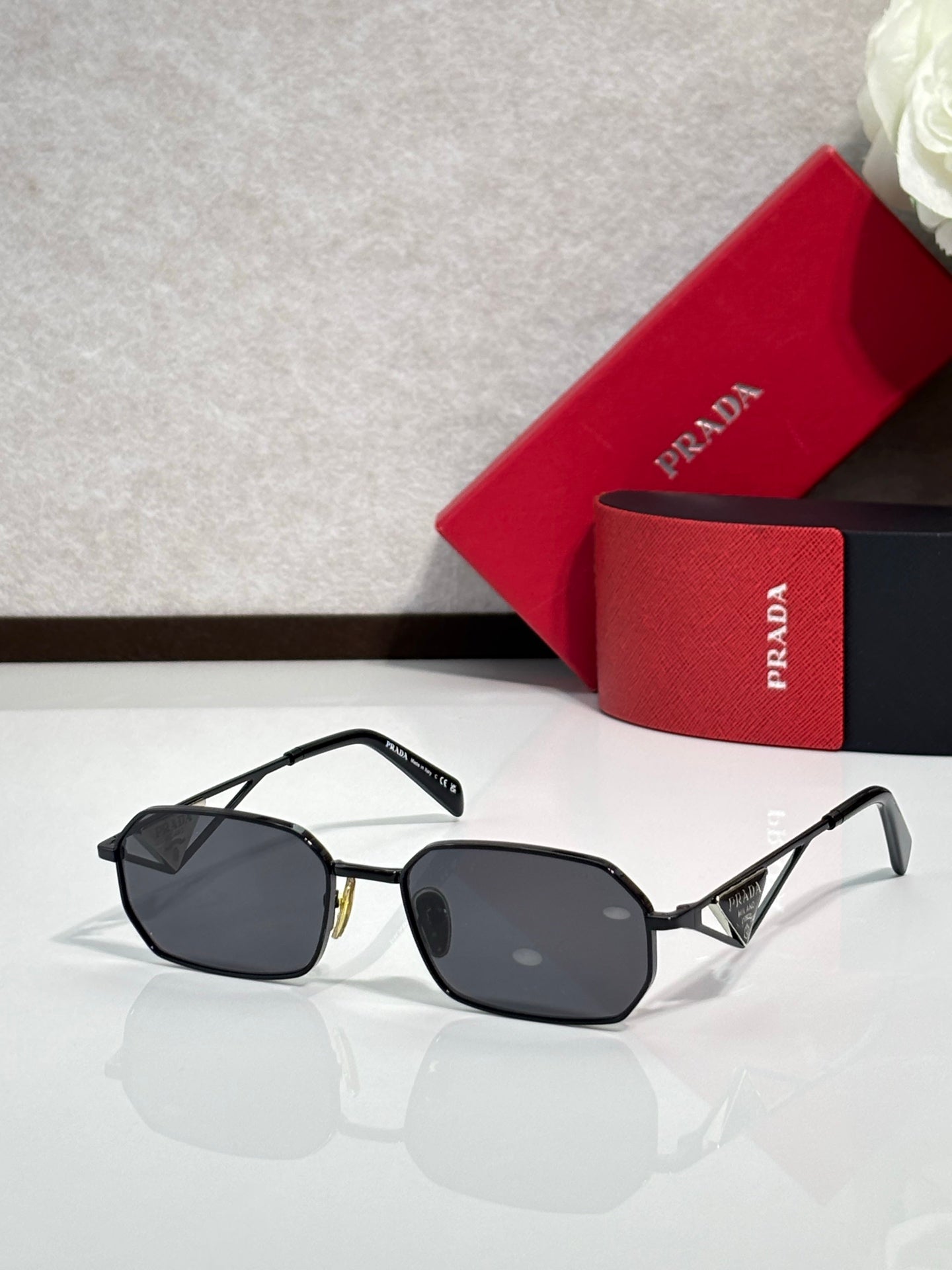 Prada sunglasses with black frame and dark tinted lenses, beside a red logo case.