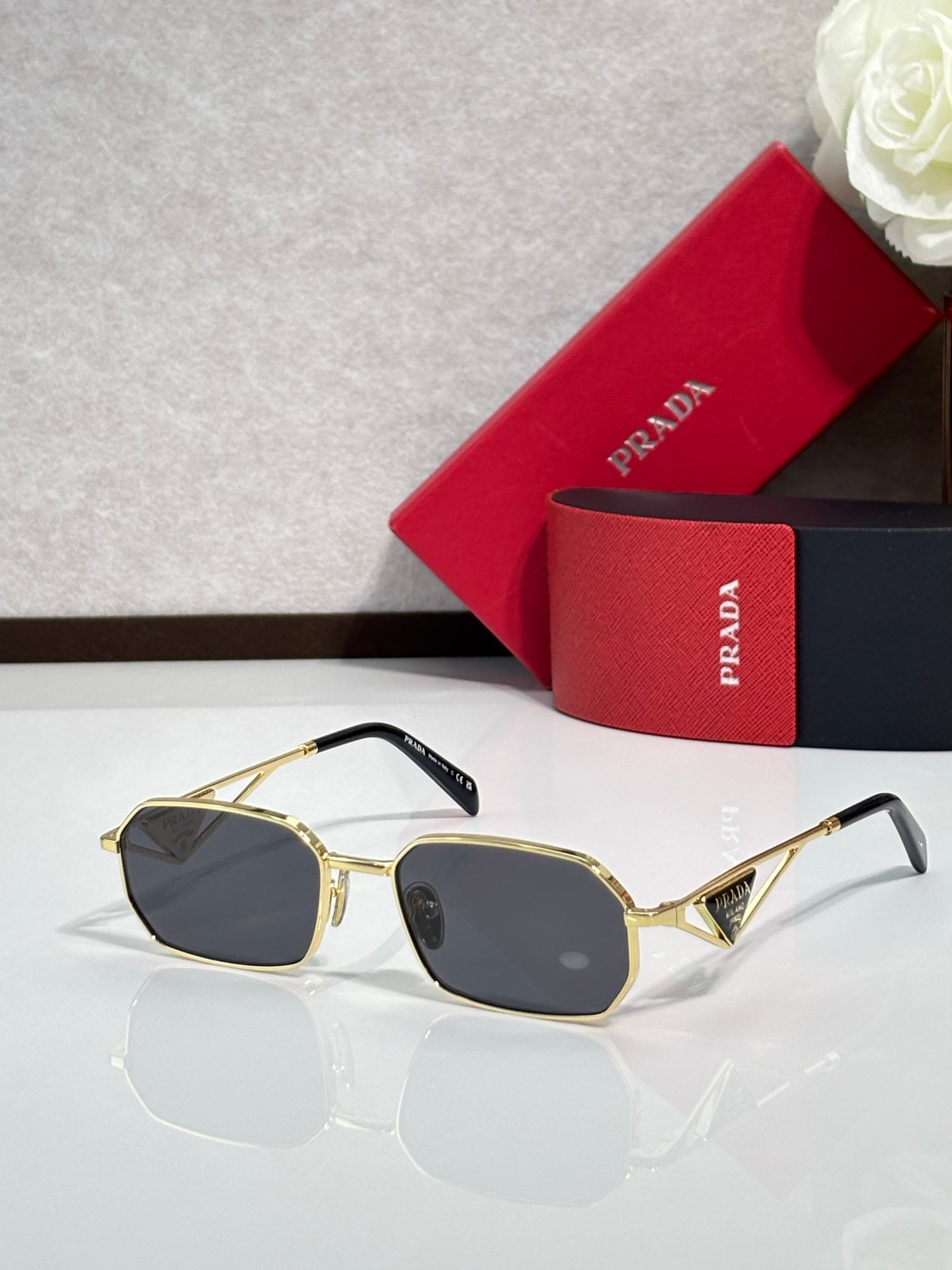 Prada sunglasses with gold frame and dark tinted lenses, with a red logo case.