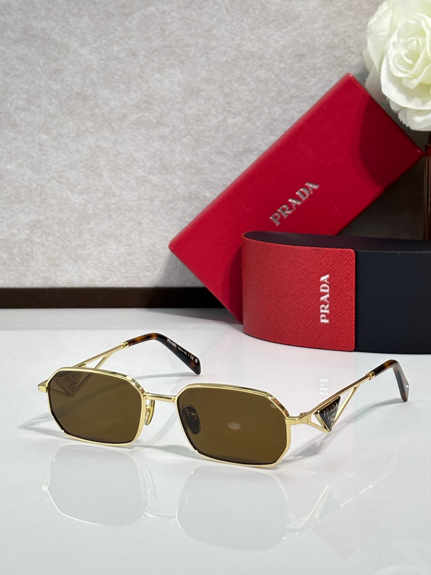 Prada sunglasses with gold frame and brown tinted lenses, with a red and navy logo case.