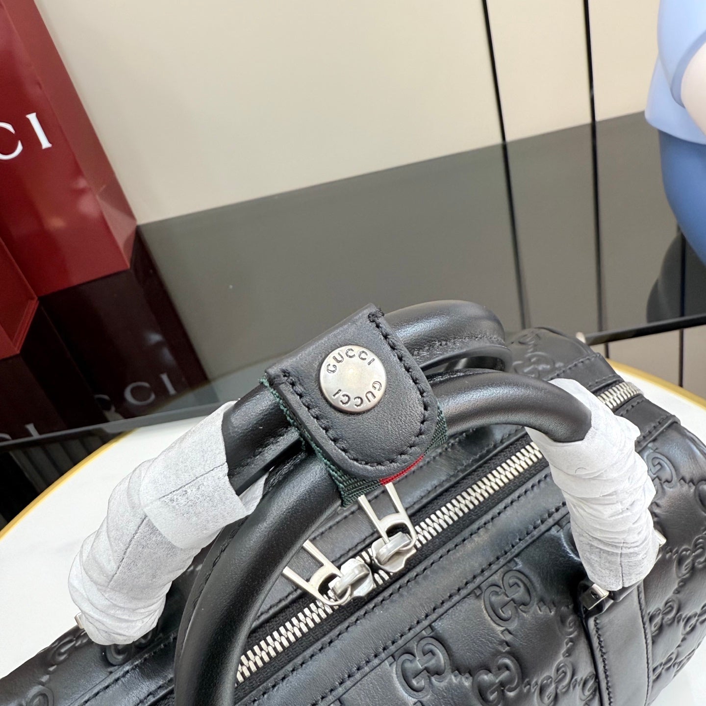 Handbag handle detail with Gucci stamp and zipper pull on dark gray GG leather