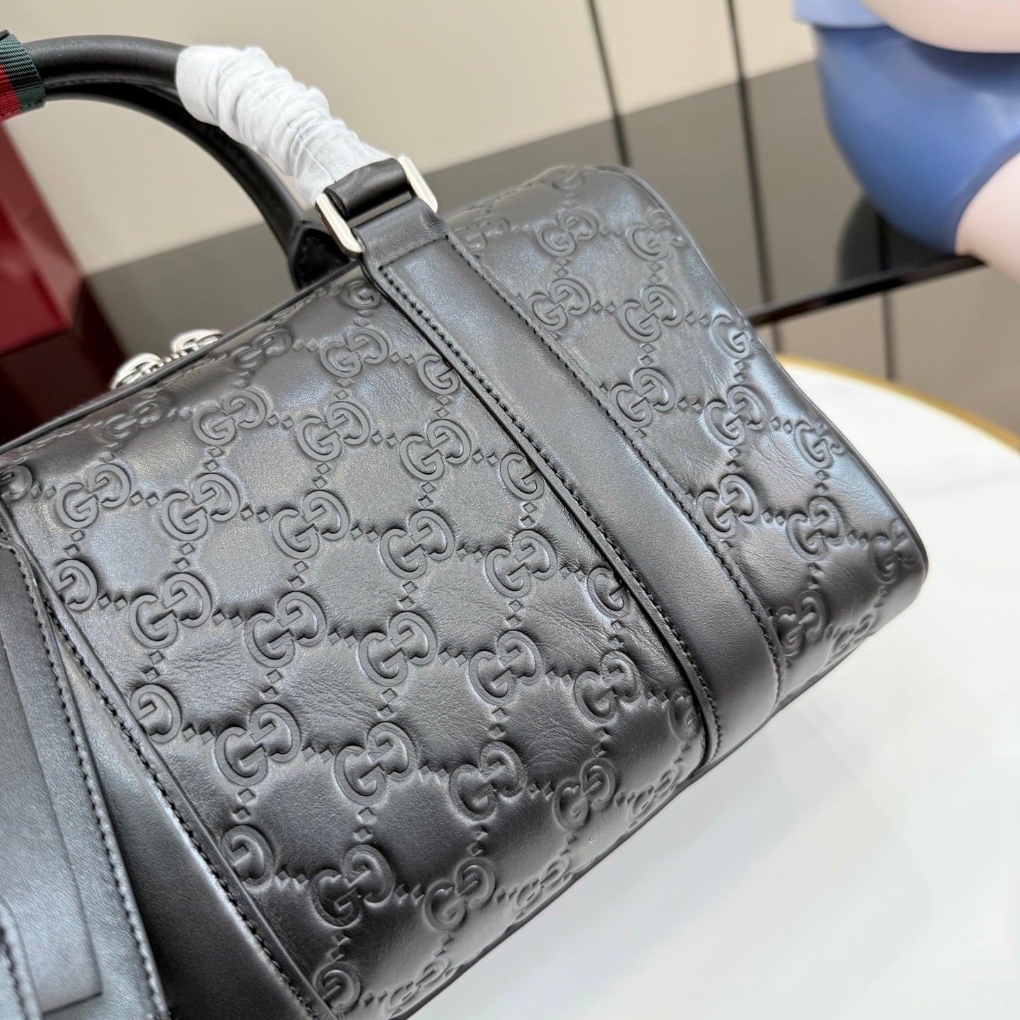 Dark gray GG monogram handbag side with stitched leather trim and top handle