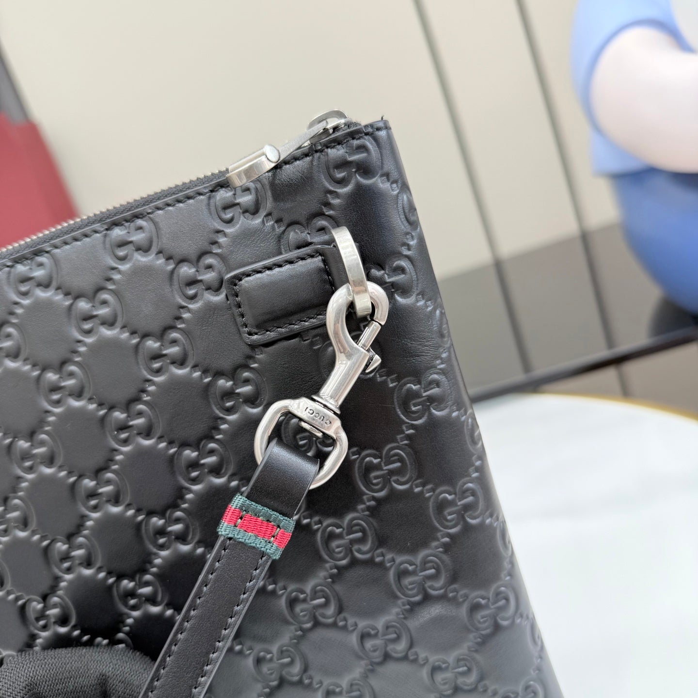 Gucci GG monogram pouch bag close-up of metal keyring and strap detail.