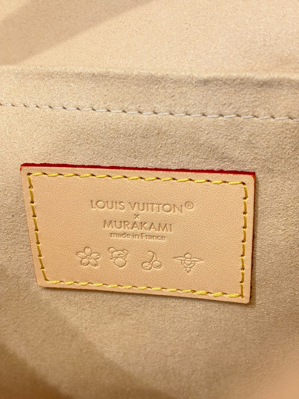 Leather brand patch reading Louis Vuitton MURAKAMI on beige background with embossed icons