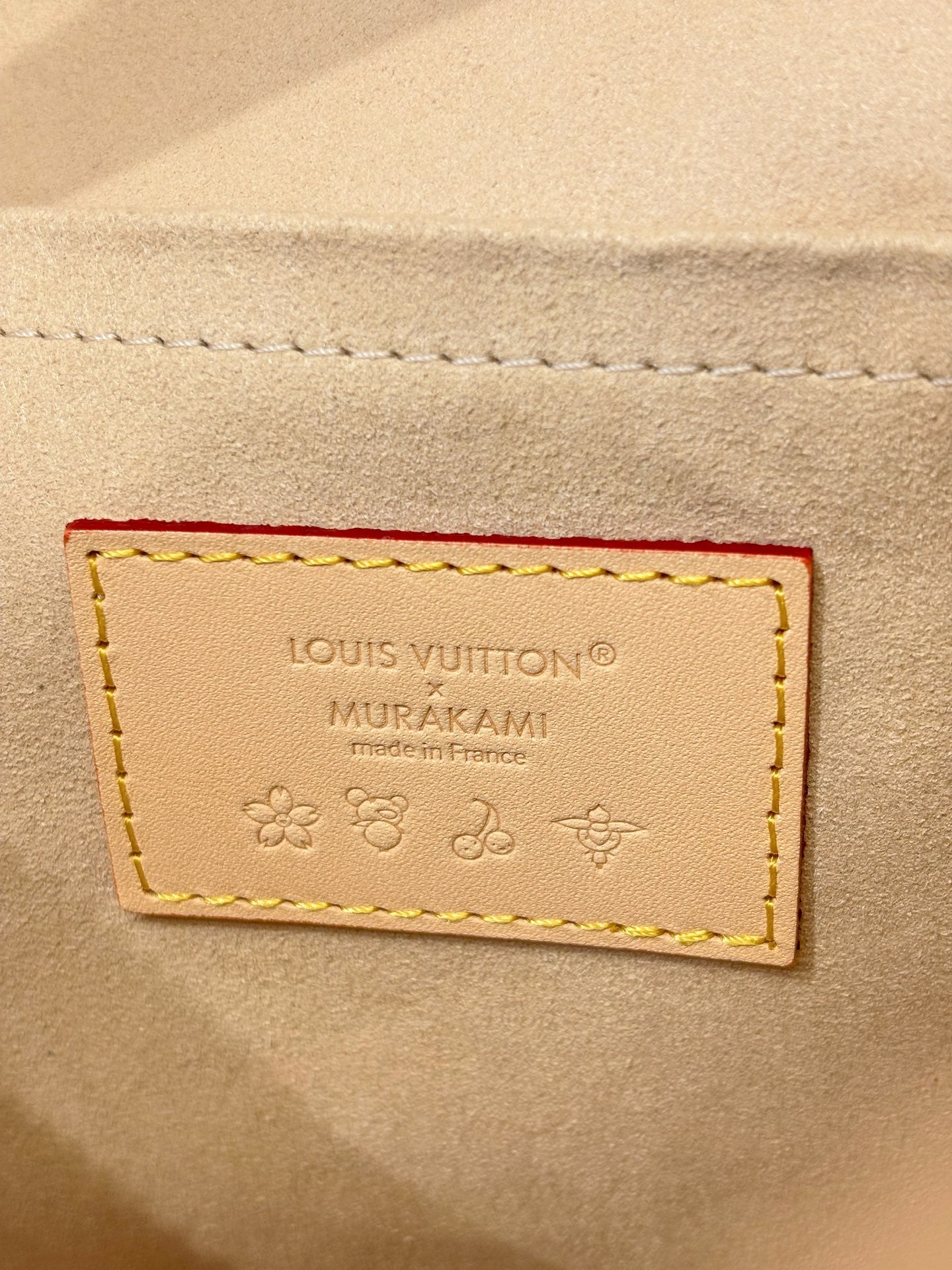 Leather brand patch reading Louis Vuitton MURAKAMI on beige background with embossed icons