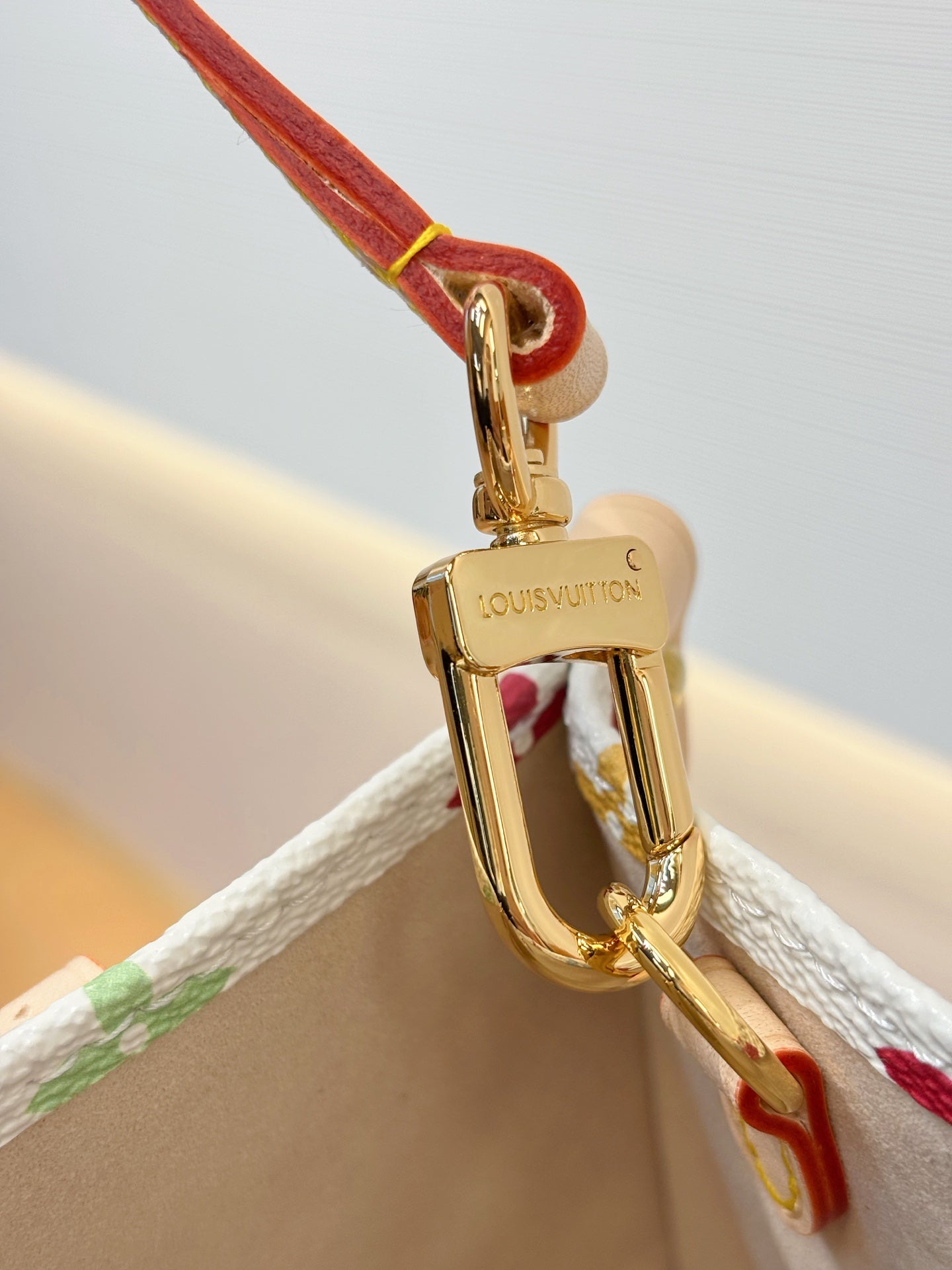 Gold-tone clasp on multicolor monogram bag with red strap loop
