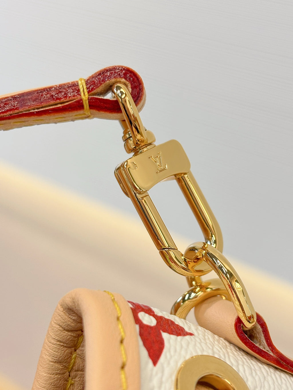 Louis Vuitton bag close-up of gold chain clasp with “LV” charm and monogram strap