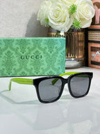 Gucci sunglasses with black frames, green temple arms, and dark lenses