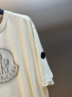 Cream T-shirt sleeve detail with black buttoned tab and partial logo print