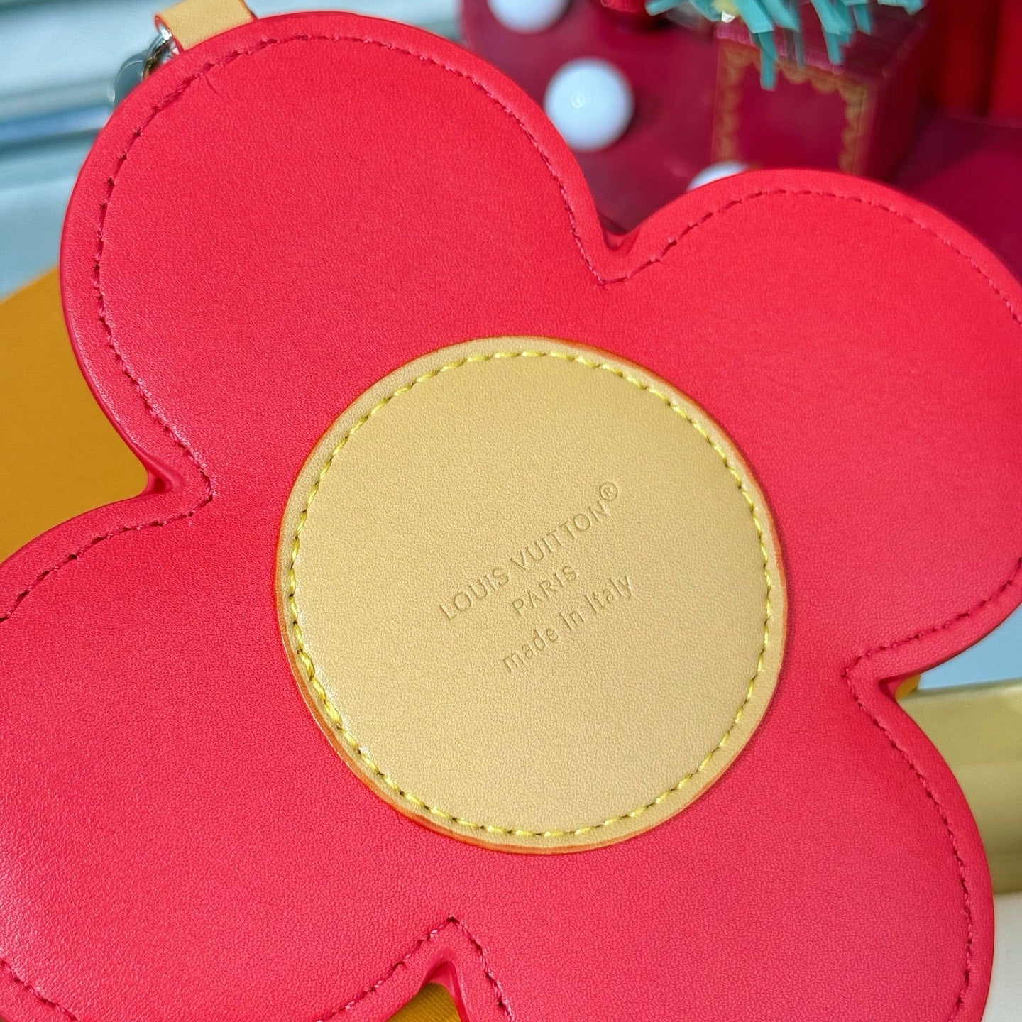 Red leather flower charm with beige center label, stitched edges, and rounded petals.