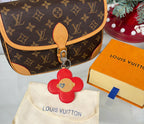 Red leather flower keychain on cream dust bag with Louis Vuitton lettering.