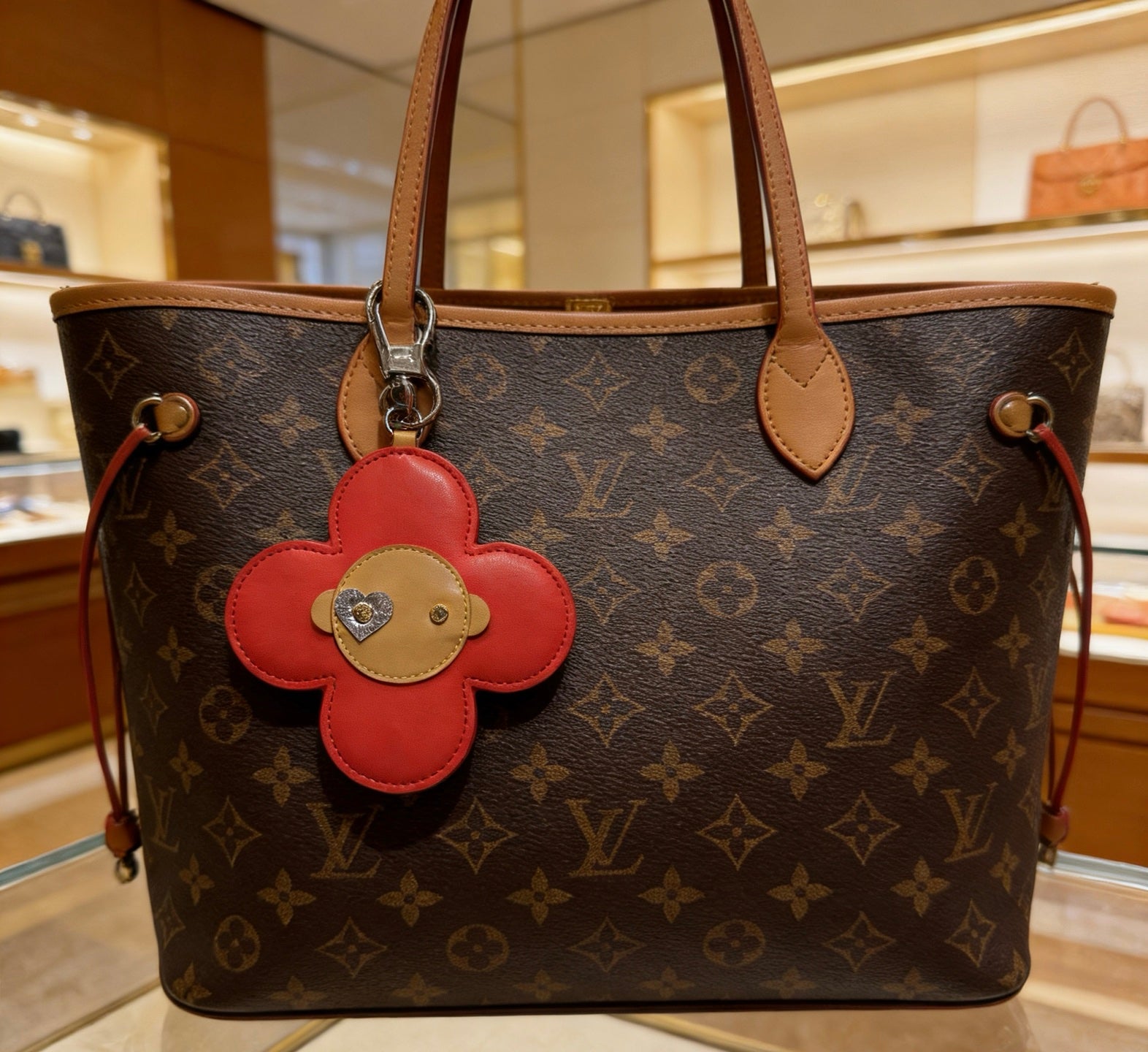 Red leather flower bag charm with beige center and heart stud on monogram tote.