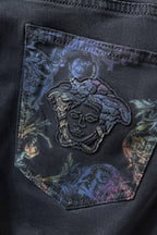 Embroidered graphic patch on dark denim pocket with ornate blue and gold accents