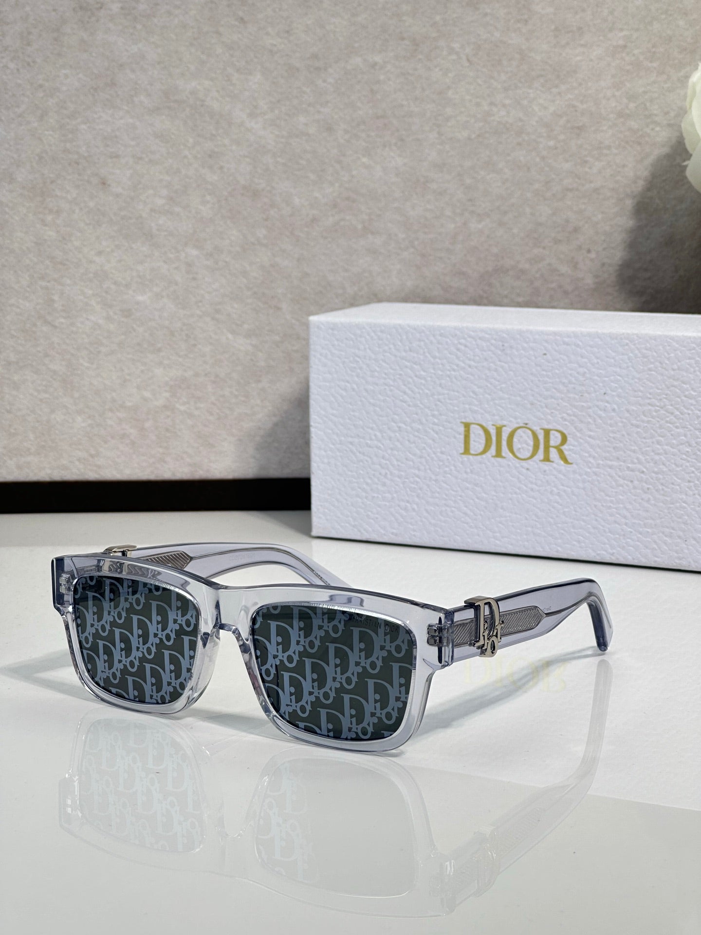 Clear gray square sunglasses with dark monogram lenses and gold logo bar.