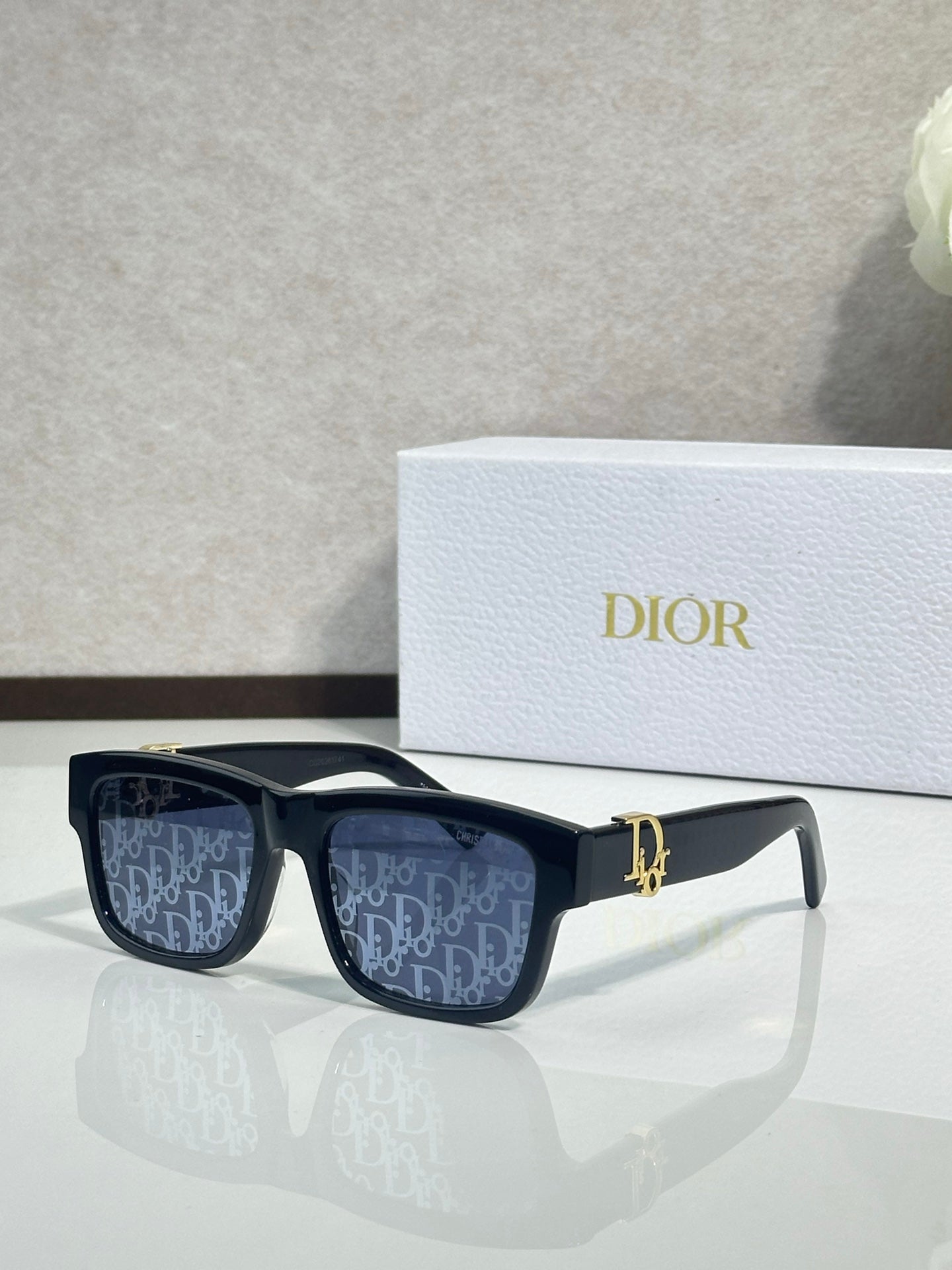 Black square sunglasses with dark monogram lenses and gold logo bar detail.