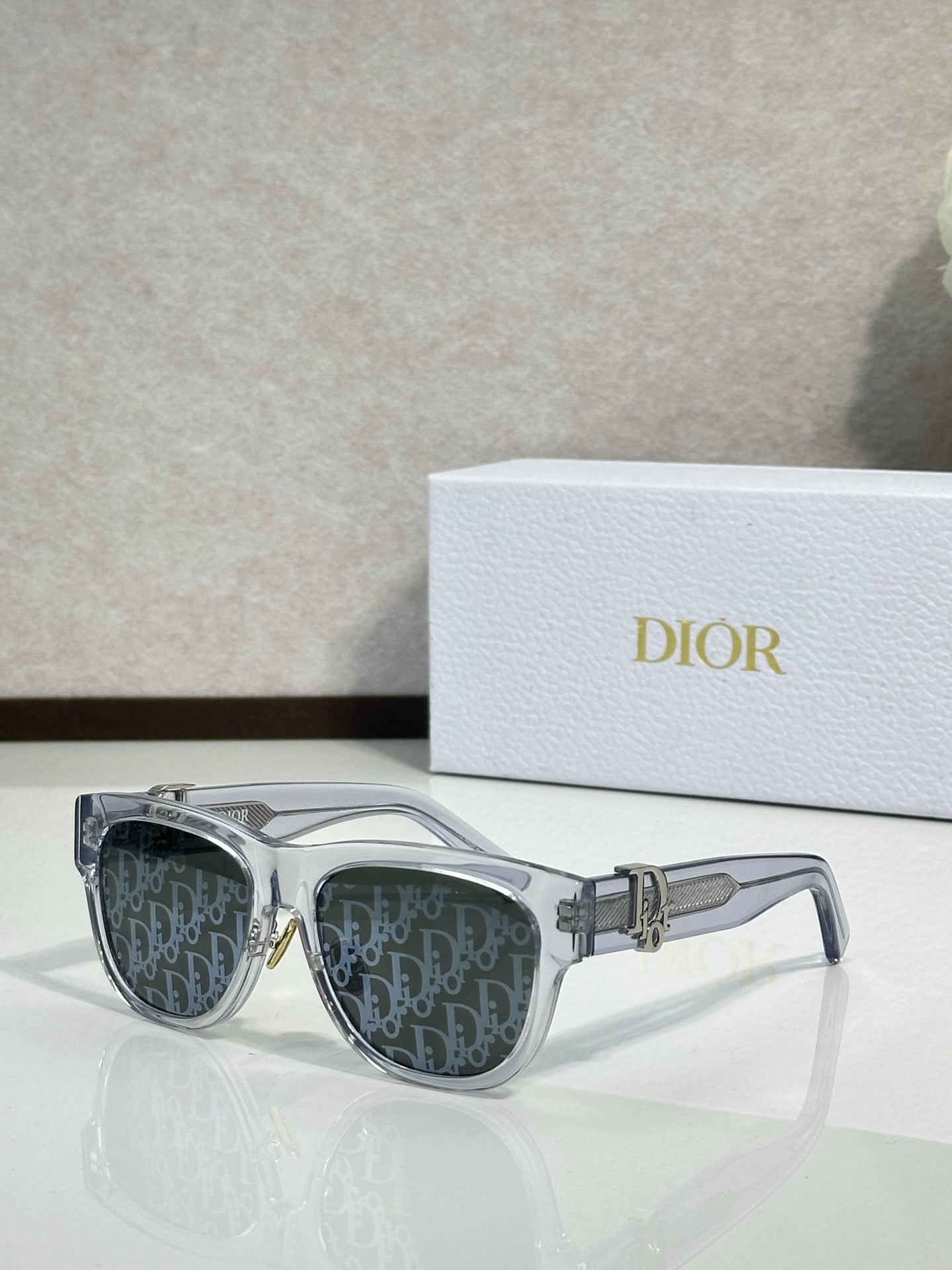 Dior sunglasses with clear gray frames, dark lenses, and gold side logo detail