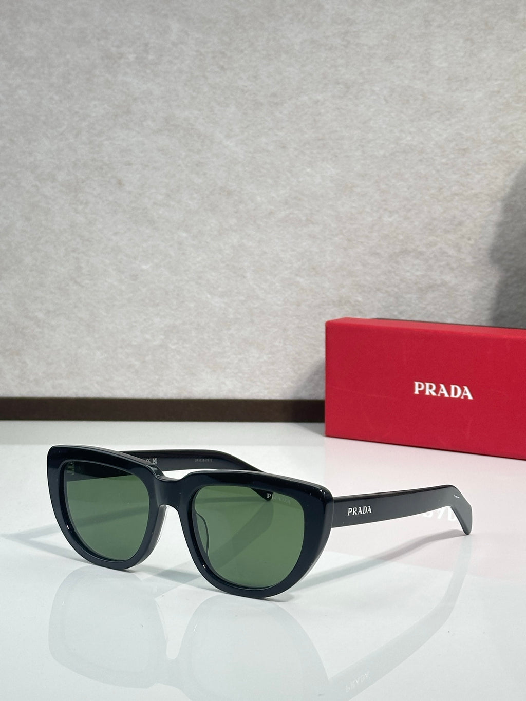 Prada sunglasses with black frames and green-tinted lenses, angled side view