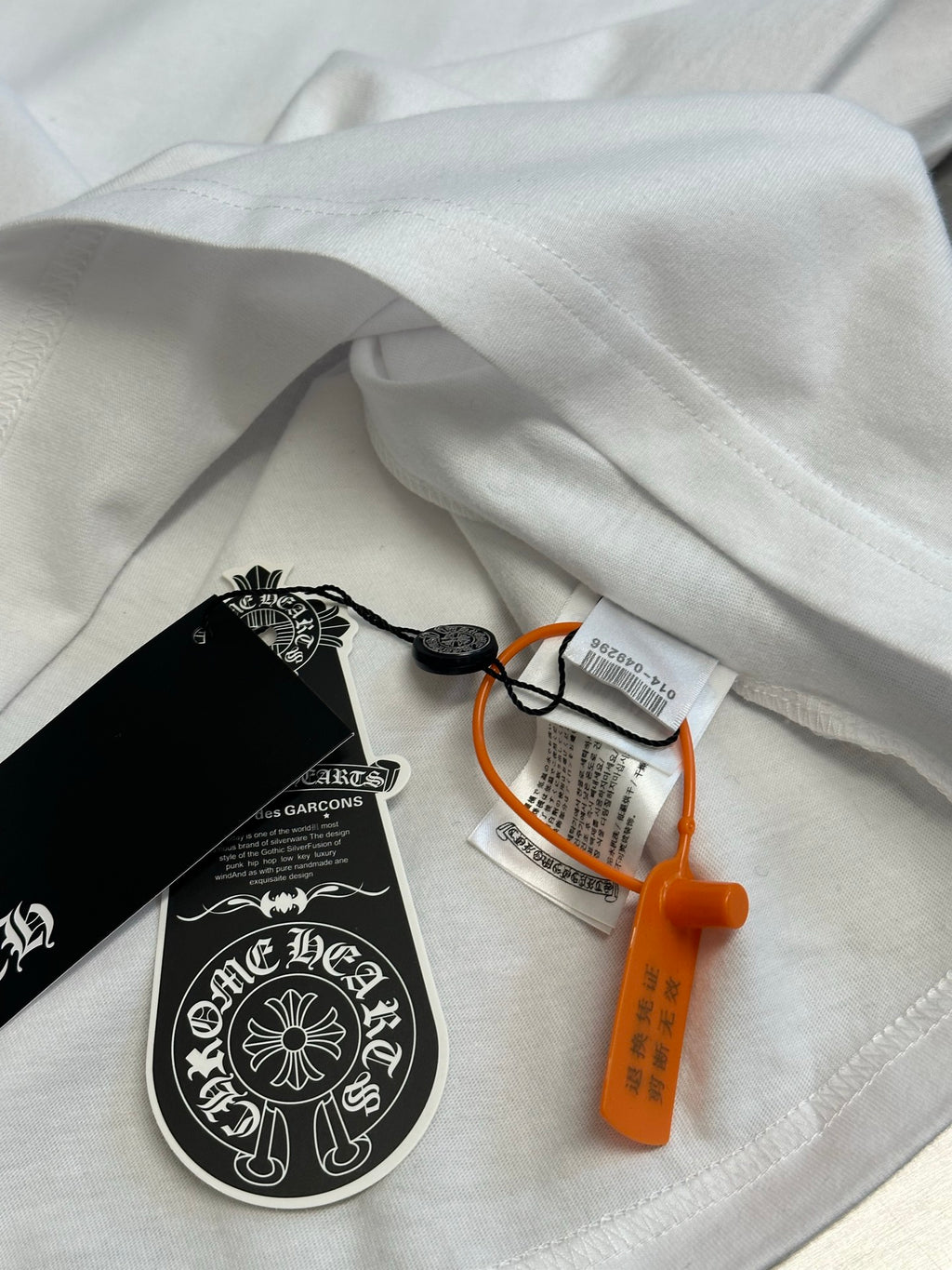Folded white T-shirt with hang tag and orange security tag on fabric