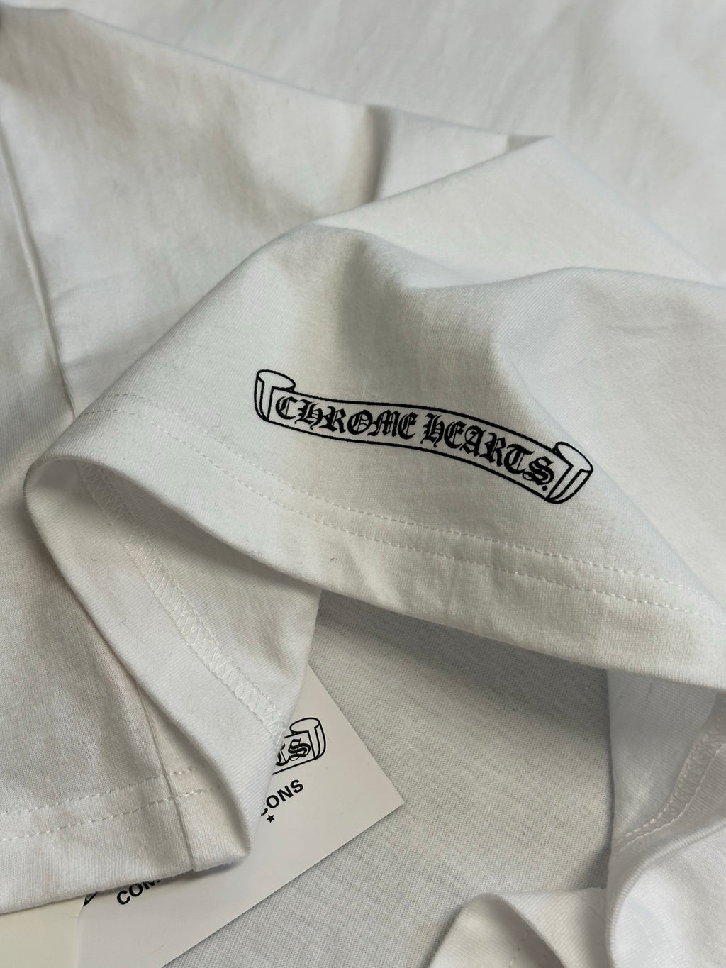 White T-shirt sleeve with Chrome Hearts logo graphic and hanging label