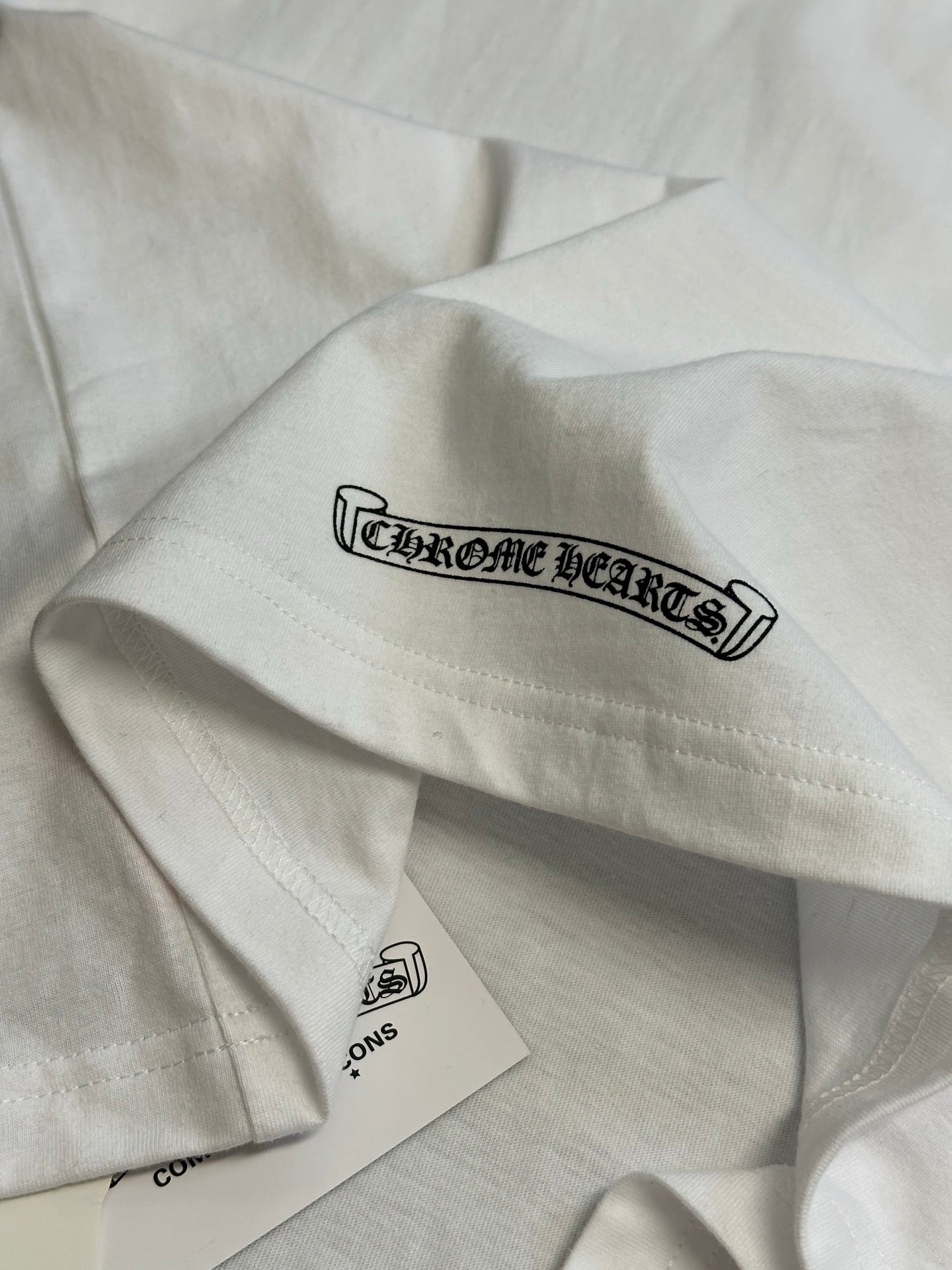 White T-shirt sleeve with Chrome Hearts logo graphic and hanging label