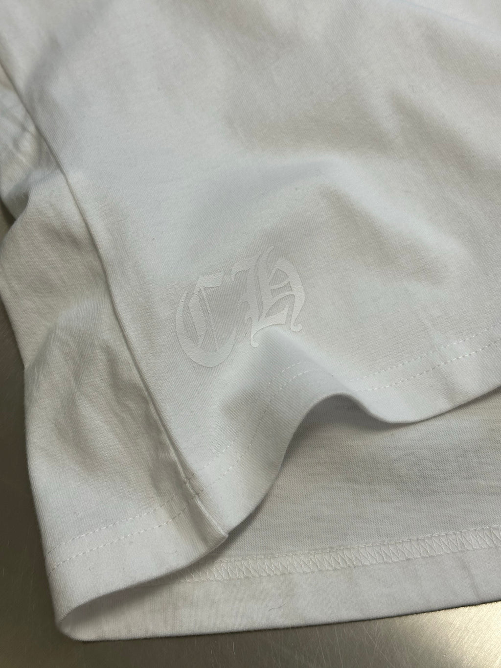 White T-shirt fabric with small embossed heart emblem near seam