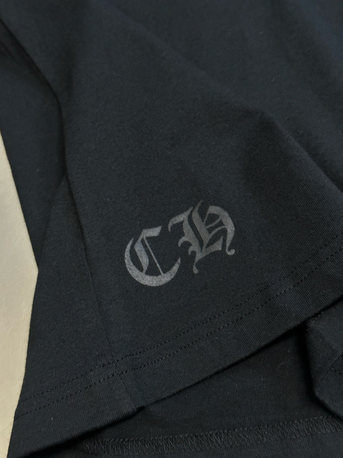 Black T-shirt sleeve hem with small gray logo patch stitching detail