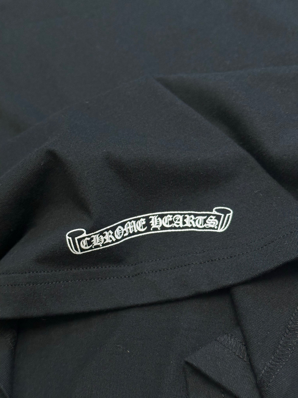 Black T-shirt with centered white logo patch across chest near hem