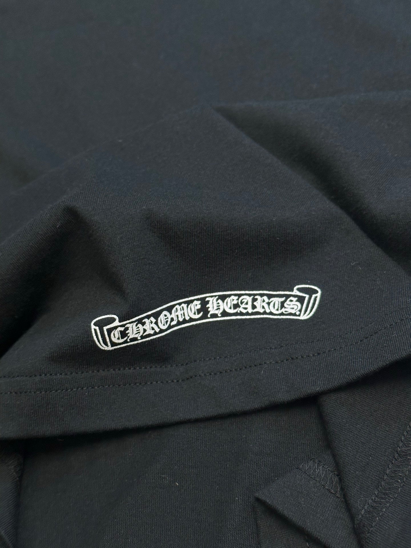 Black T-shirt with centered white logo patch across chest near hem