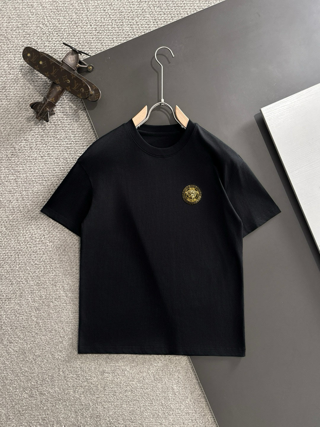 Black short-sleeve T-shirt with small gold crest logo