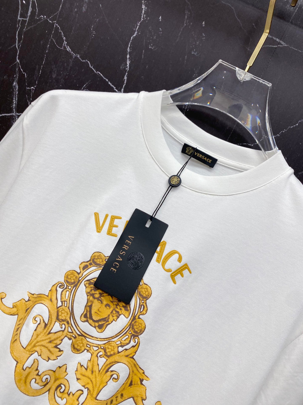 White T-shirt with gold crest print, VERSACE text, and hanging tag